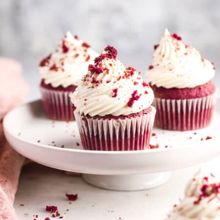 Three red velvet cupcakes on a white cake stand.