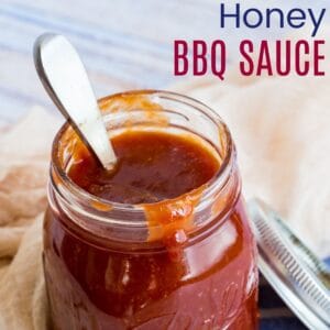 spoon in ajar of honey barbecue sauce with some dripping over the side