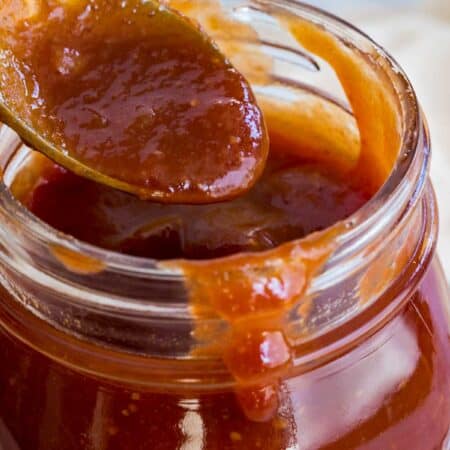 honey bbq sauce dripping off of a spoon into jar with more sauce dripping on the rim