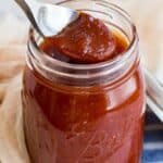 spoon picking up honey bbq sauce out of a glass jar