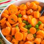 honey dijon peas and carrots in a white bowl on top of a striped napkin and a piece of burlap