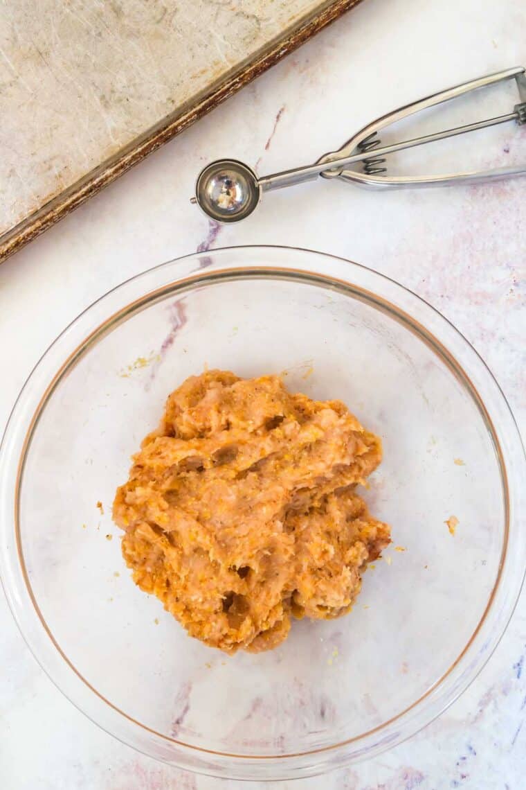 raw turkey mixture in a bowl next to a scoop and a baking sheet