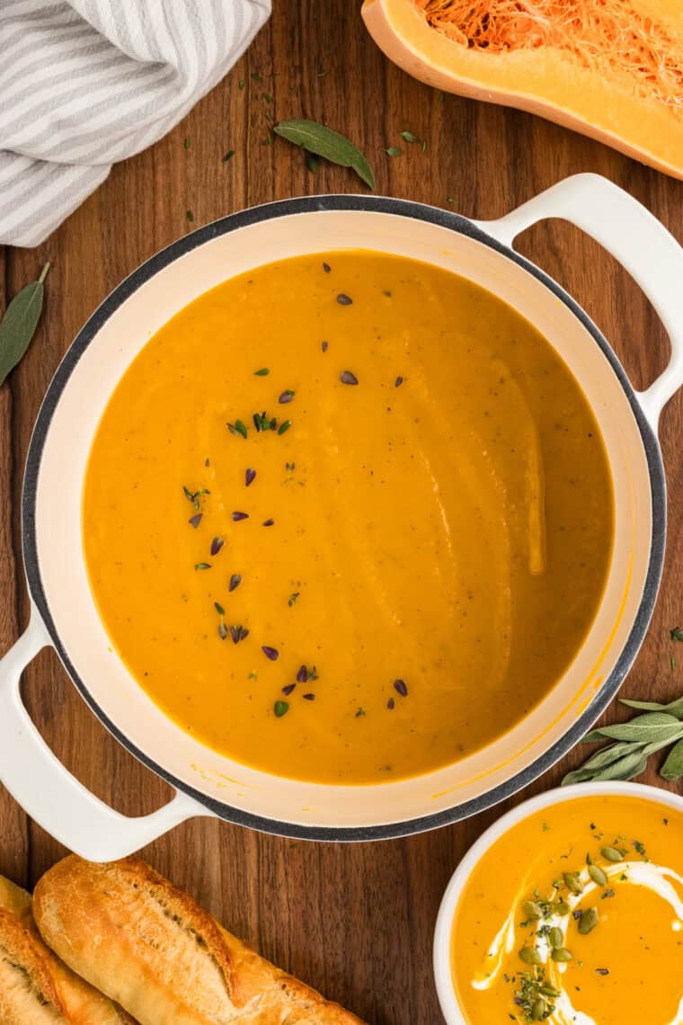 Overhead view of a pot of butternut squash soup with herbs on top.