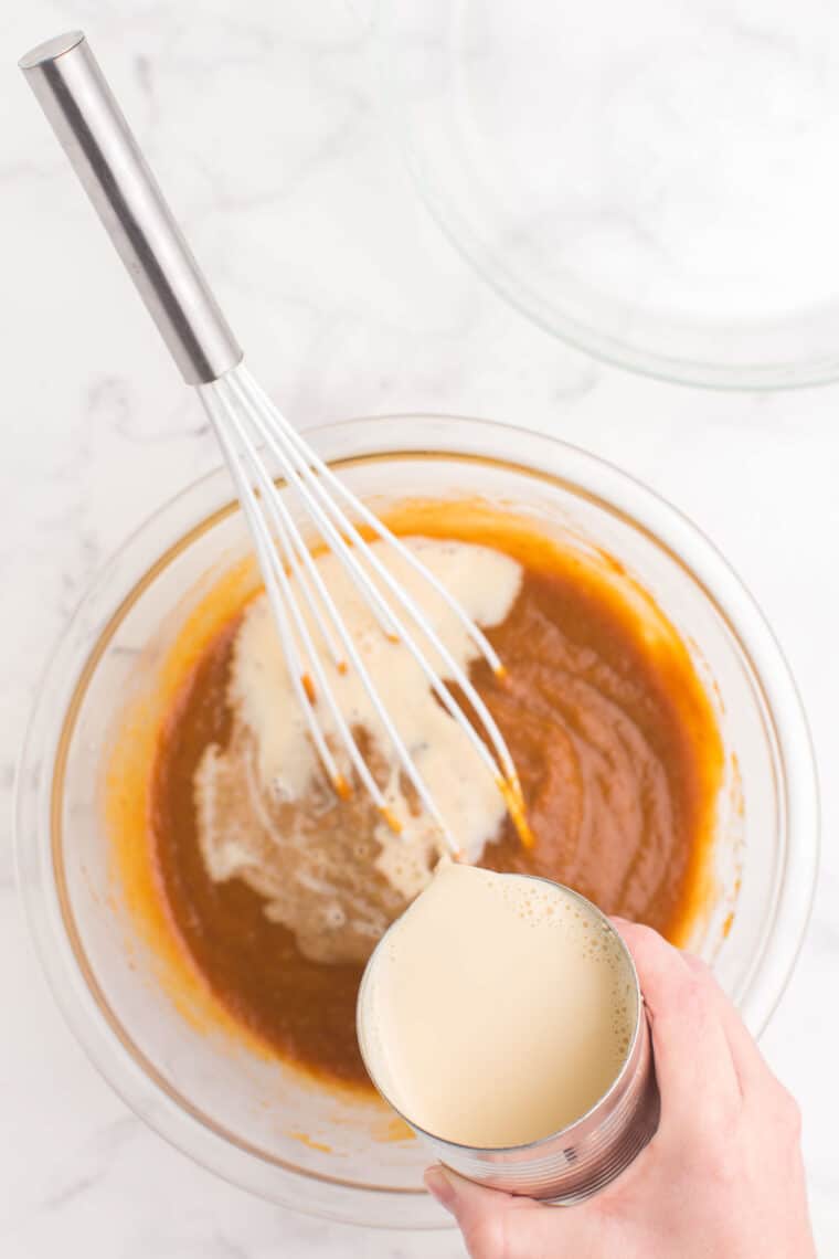 pouring a can of evaporated milk into a glass bowl with the pumpkin mixture