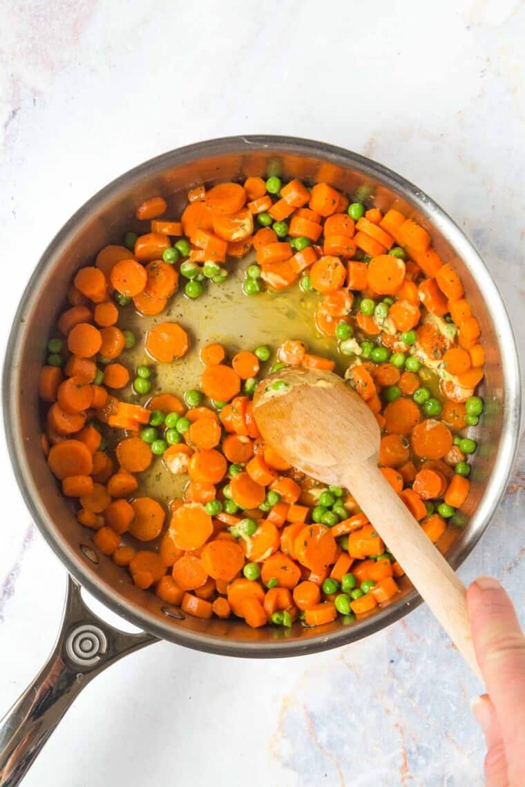 using a wooden spoon to stir the dijon mustard and honey into the cooked carrots and peas