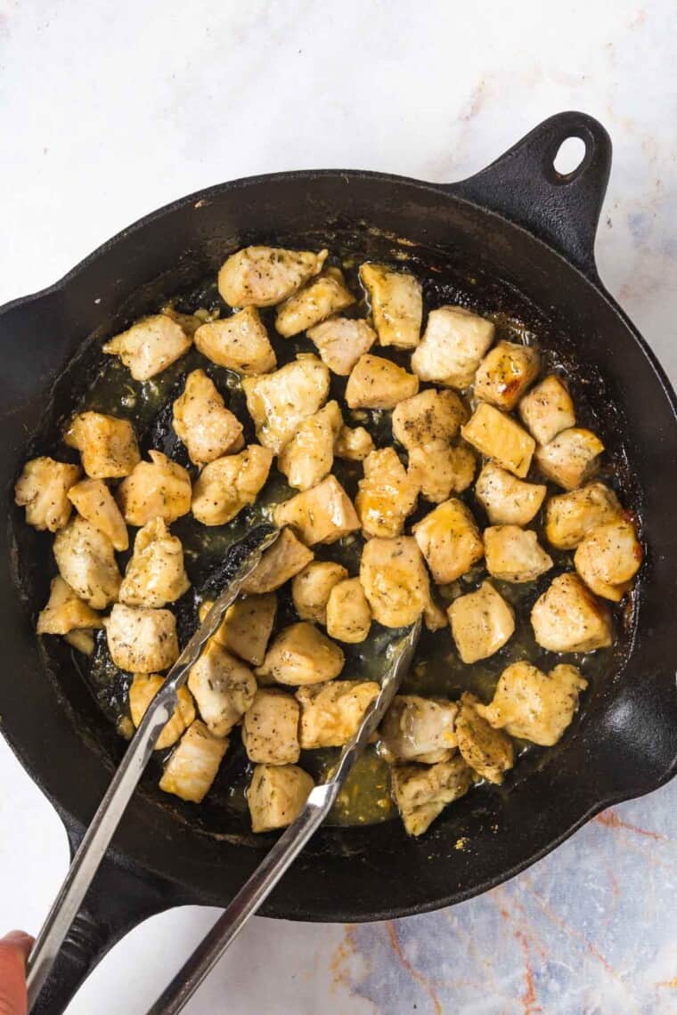 using tongs to toss the chicken bites in the glaze while still in the skillet