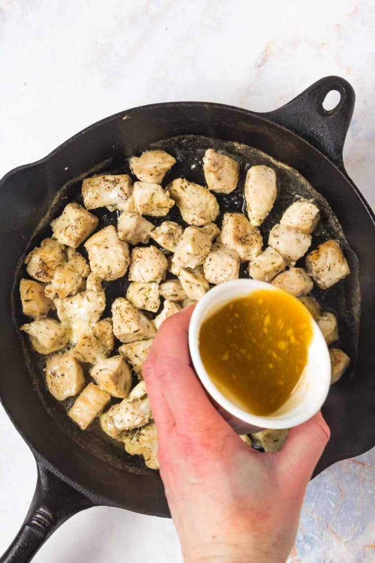 pouring honey mustard glaze over the chicken bites in a cast iron pan