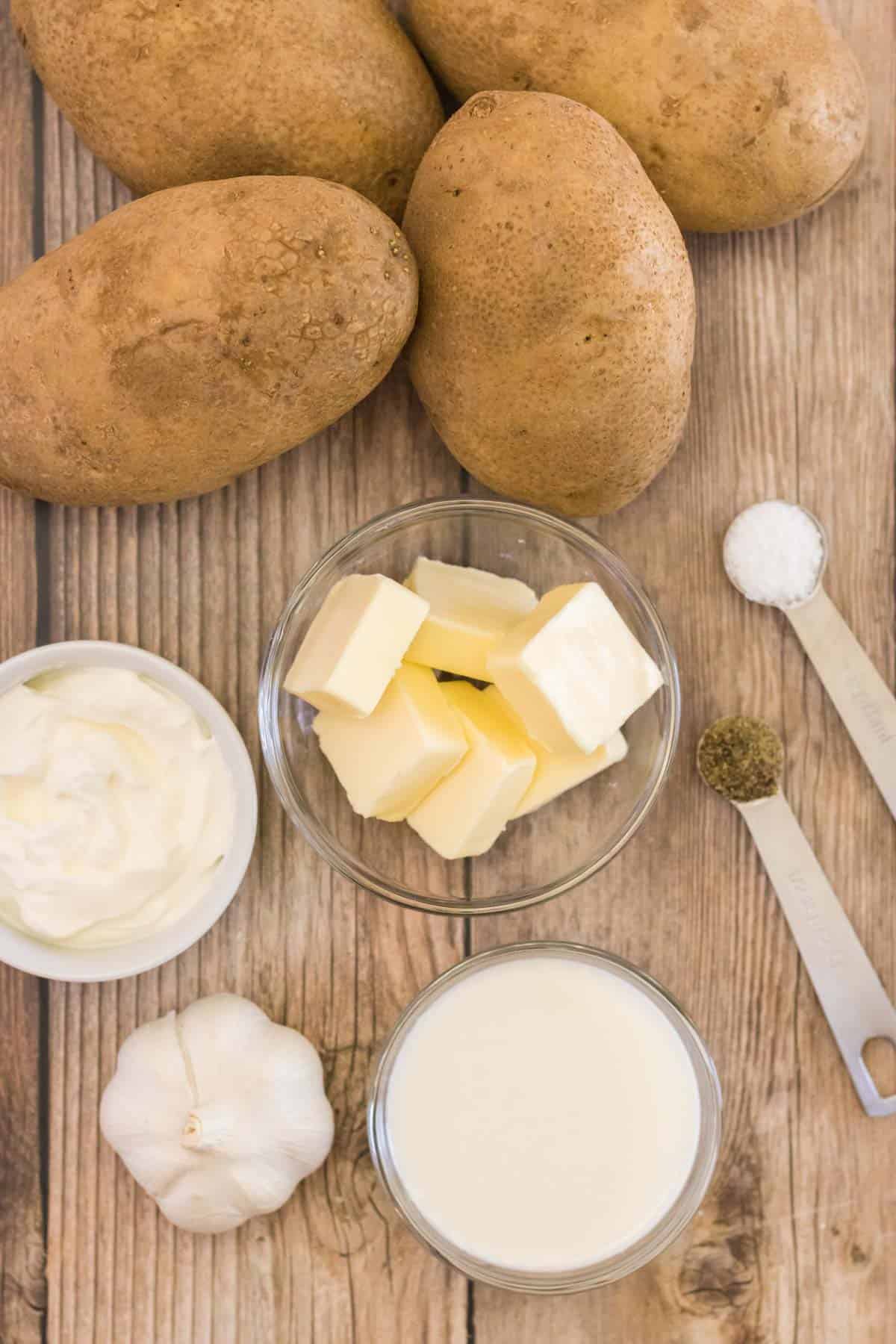 russet potatoes, butter, sour cream, garlic, salt and pepper on a cutting board