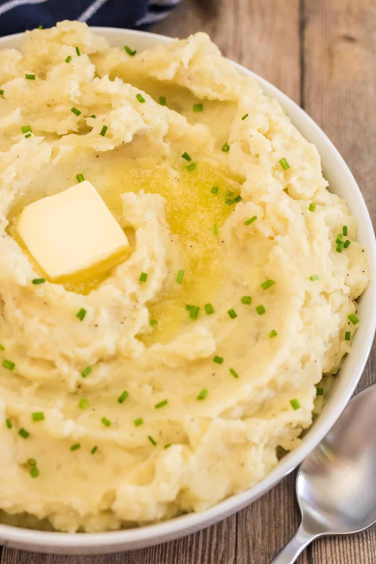 A closeup of a bowl of mashed potatoes with a pat of butter melting on top.