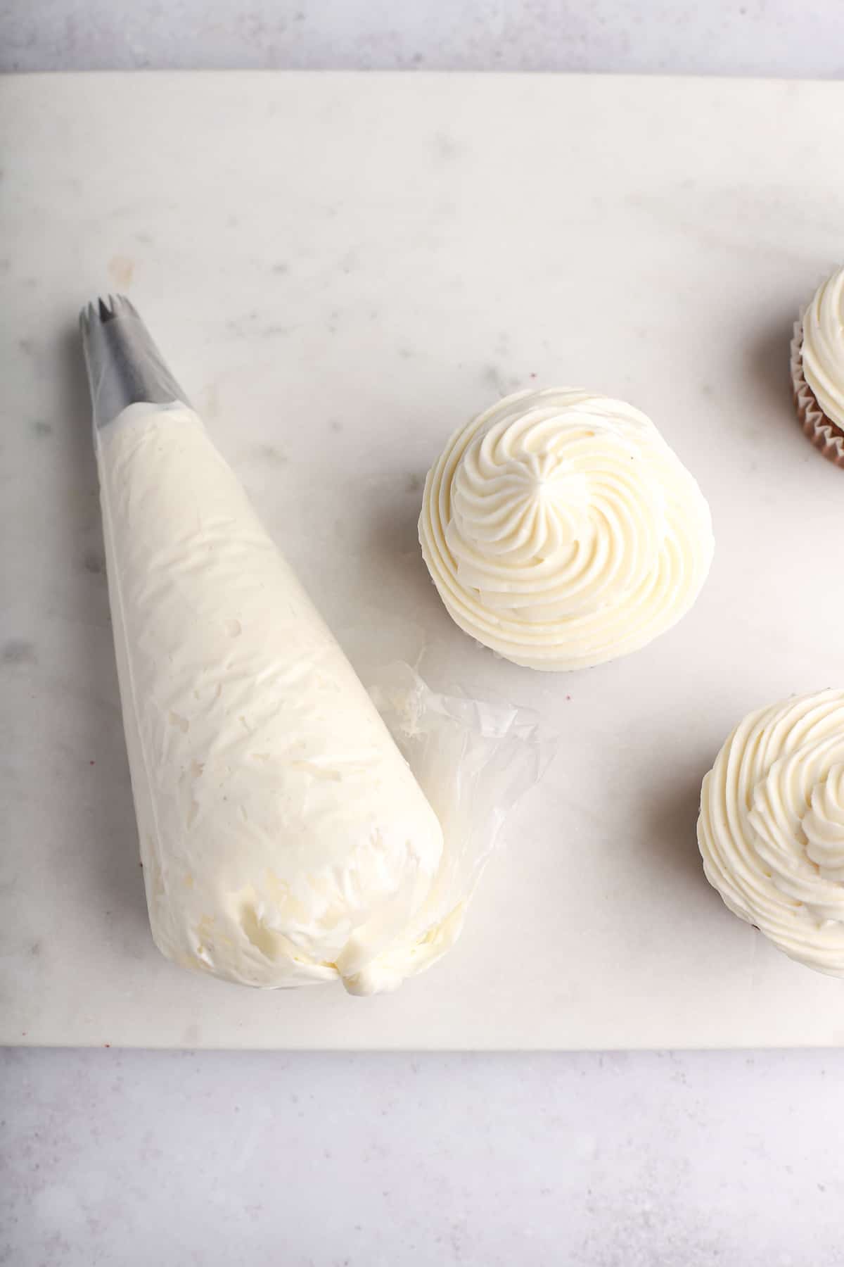 piping bag of cream cheese frosting with cupcakes