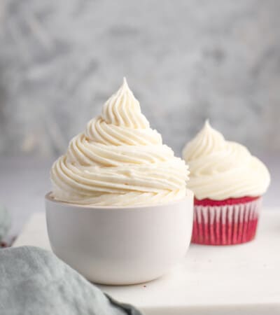 white bowl of vanilla cream cheese frosting with a cupcake in the background