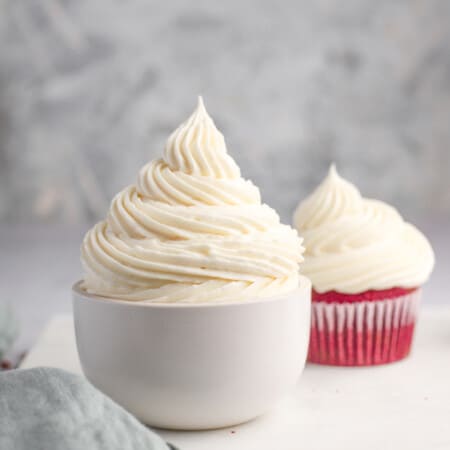 white bowl of vanilla cream cheese frosting with a cupcake in the background