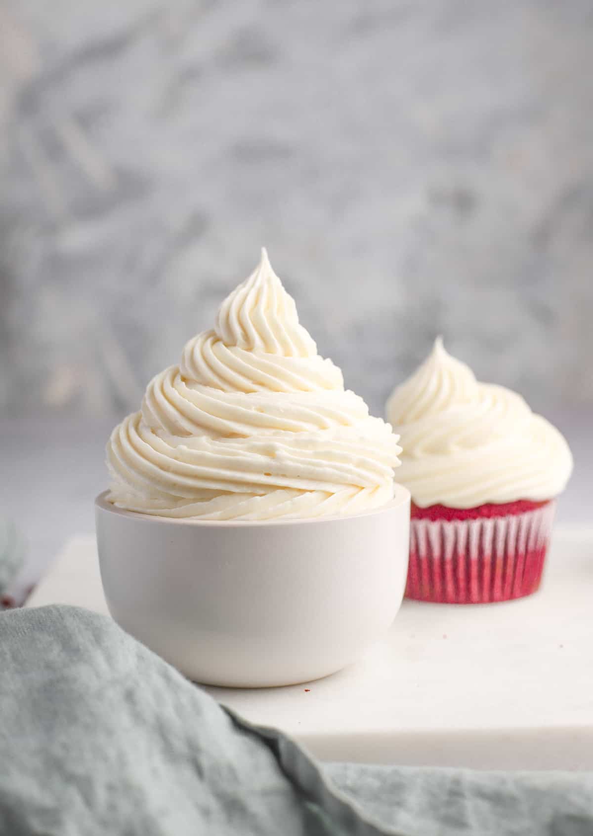 white bowl of vanilla cream cheese frosting with a cupcake in the background