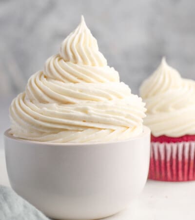 cream cheese frosting piped in a bowl and on a red velvet cupcake