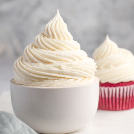 cream cheese frosting piped in a bowl and on a red velvet cupcake