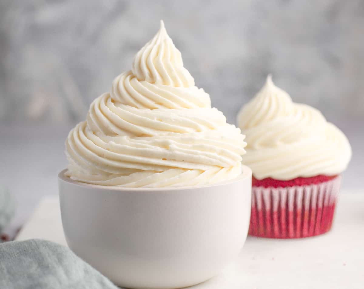 cream cheese frosting piped in a bowl and on a red velvet cupcake