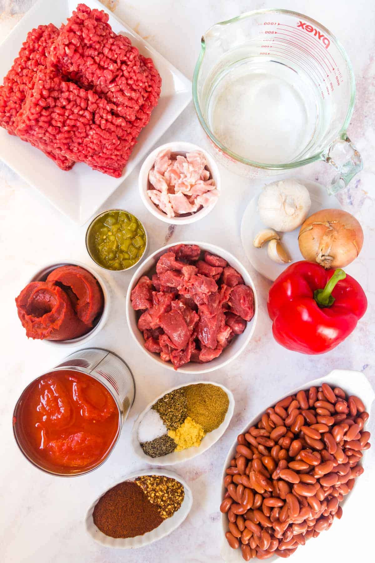 Ingredients for beef chili in white bowls, including beans, beef and veggies.