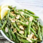 Green beans garnished with almond slices and lemon zest in a white oval dish.