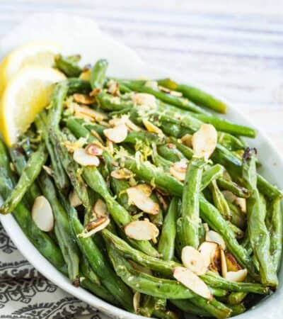 Green beans garnished with almond slices and lemon zest in a white oval dish.