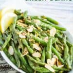 air fryer green beans with sliced toasted almonds and lemon zest plus two lemon wedges in a white serving dish