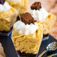 mini pumpkin parfaits with whipped cream staggered on a slate platter with a stack of mini spoons