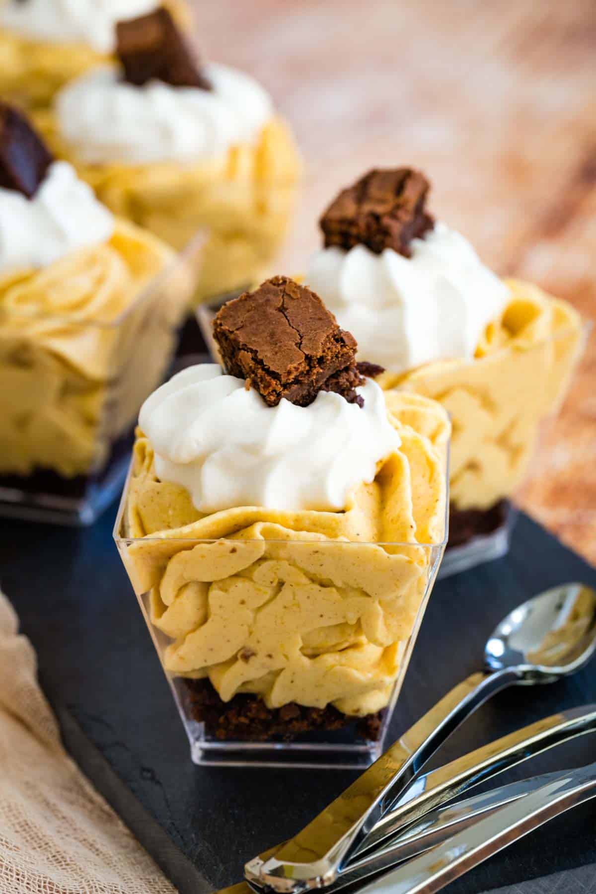 mini pumpkin parfaits with whipped cream staggered on a slate platter with a stack of mini spoons