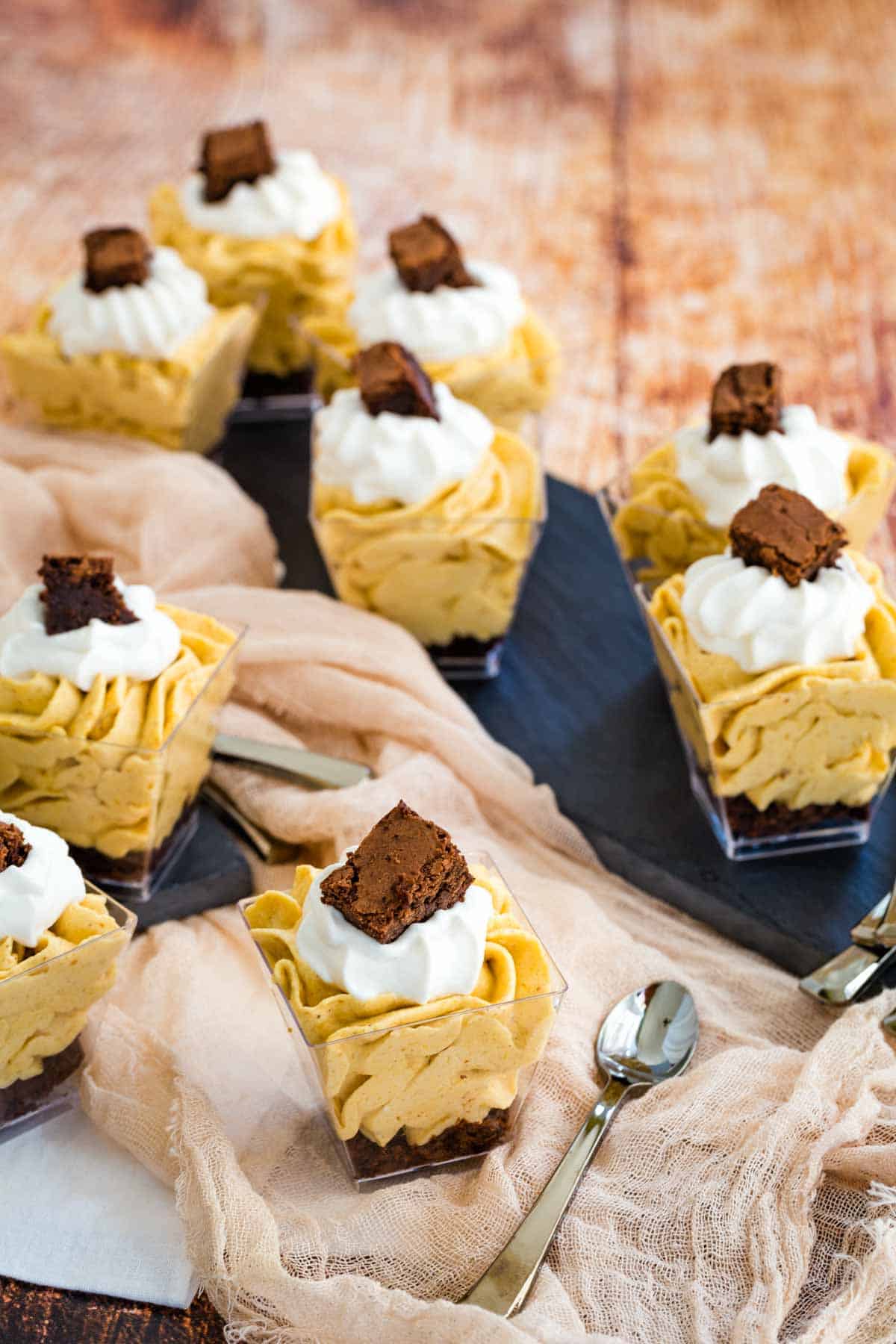 a bunch of mini pumpkin parfaits scattered around a table top with slate platters, cloth napkins and mini dessert spoons