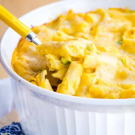 Butternut squash macaroni and cheese with peas in a white casserole dish with a serving spoon in it.