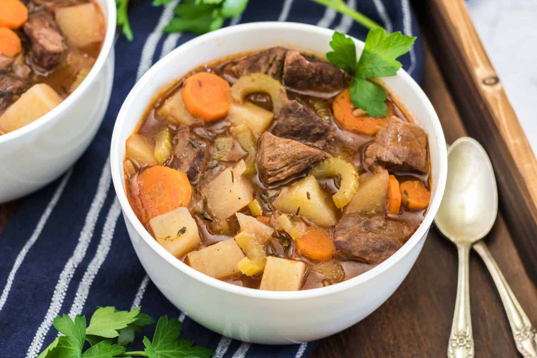 a bowl of beef stew in a white bowl garnished with parsley