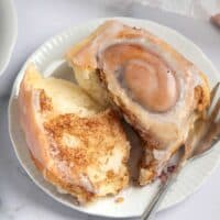 torn open gluten free cinnamon roll on a plate with a fork