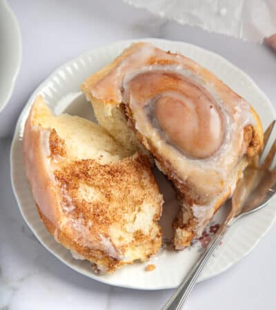 torn open gluten free cinnamon roll on a plate with a fork