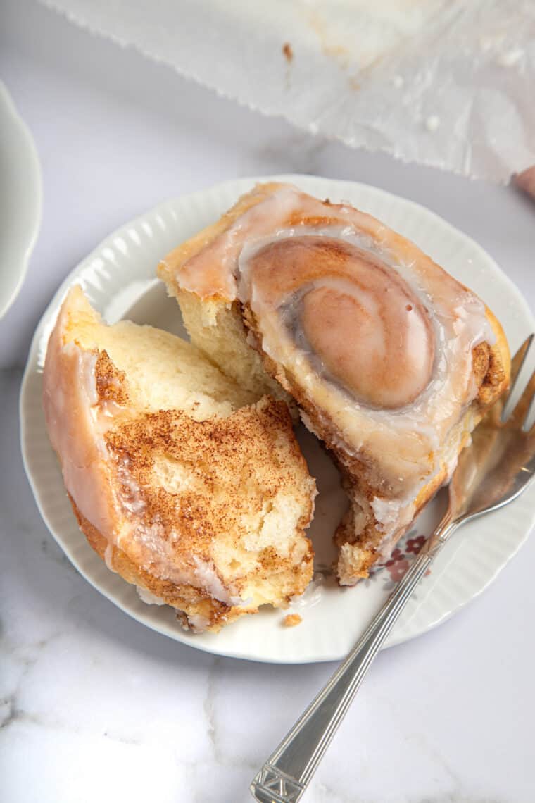 torn open gluten free cinnamon roll on a plate with a fork