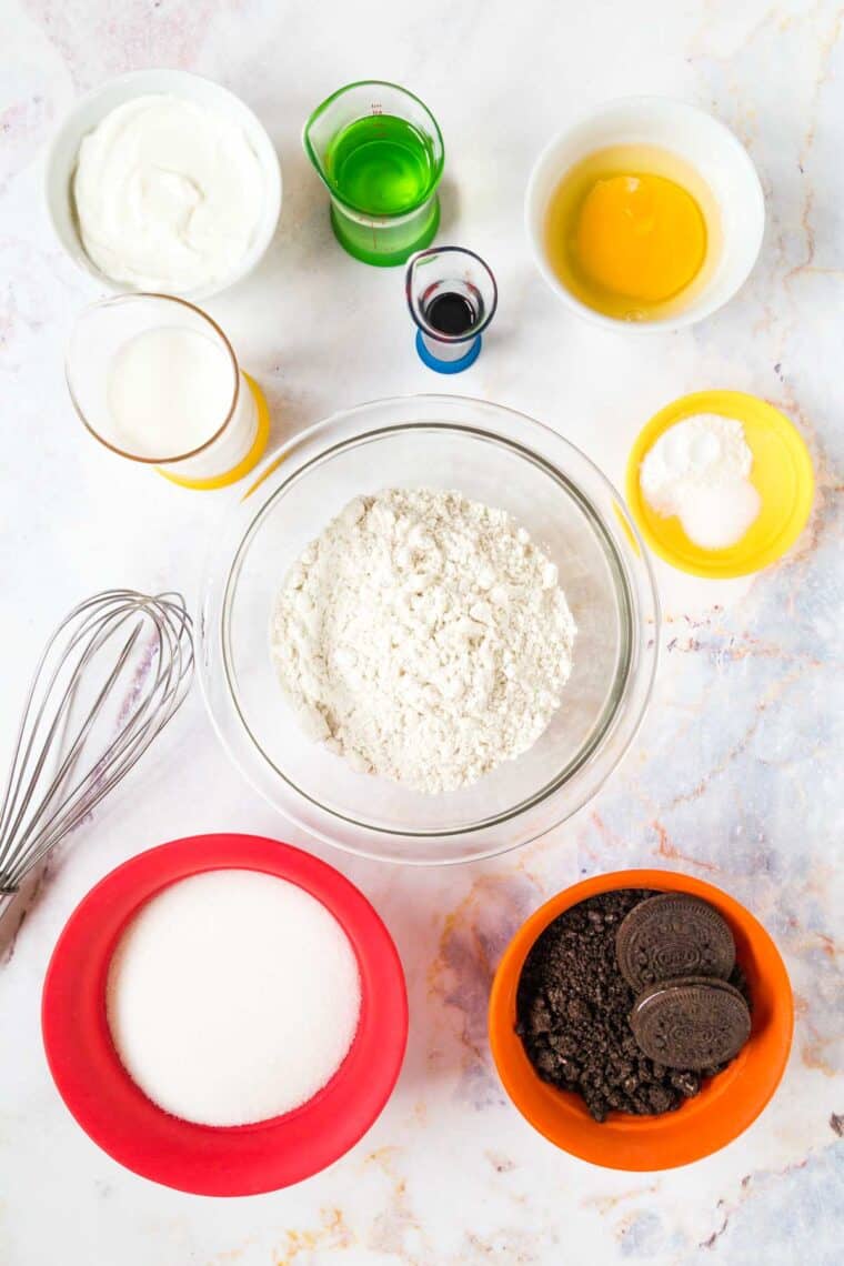 bowls of gluten free flour, sugar, chopped oreos, greek yogurt, salt, baking powder, a cracked egg, and greek yogurt, and small beakers of oil, milk, and vanilla extract