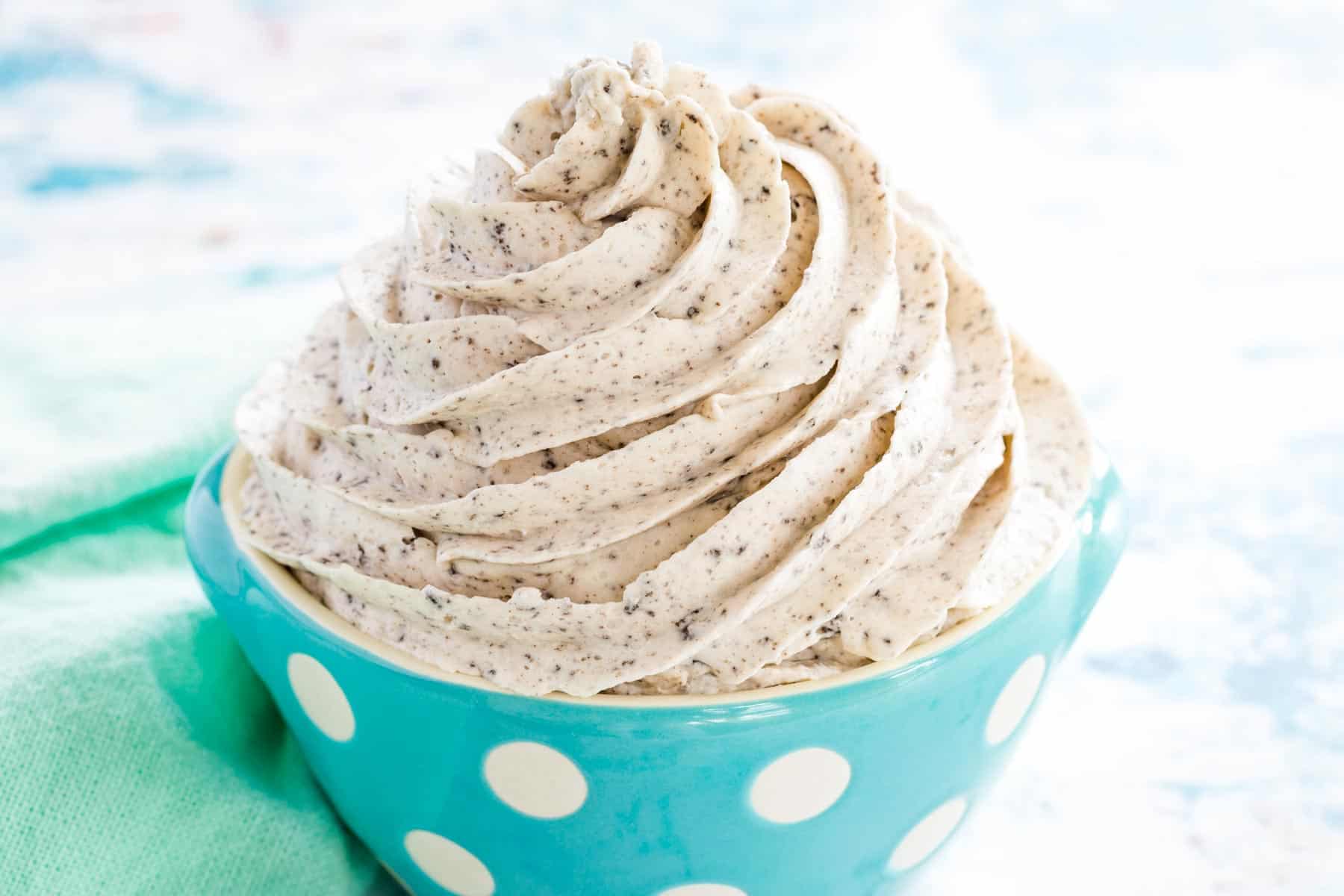 Oreo buttercream swirled in a pale blue bowl with white polka dots next to a mint green cloth napkin.