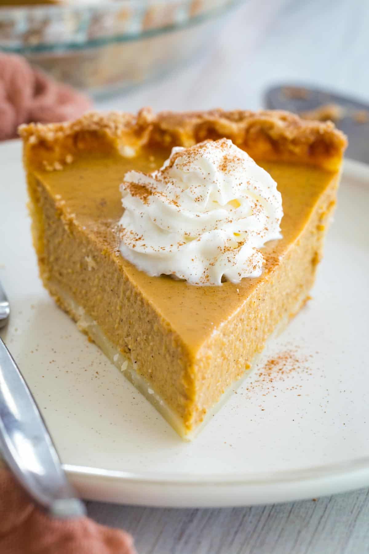 slice of pumpkin pie on a white plate with whipped cream