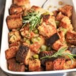 gluten free stuffing made with cubes of bread in a baking dish and garnished with fresh rosemary sprigs