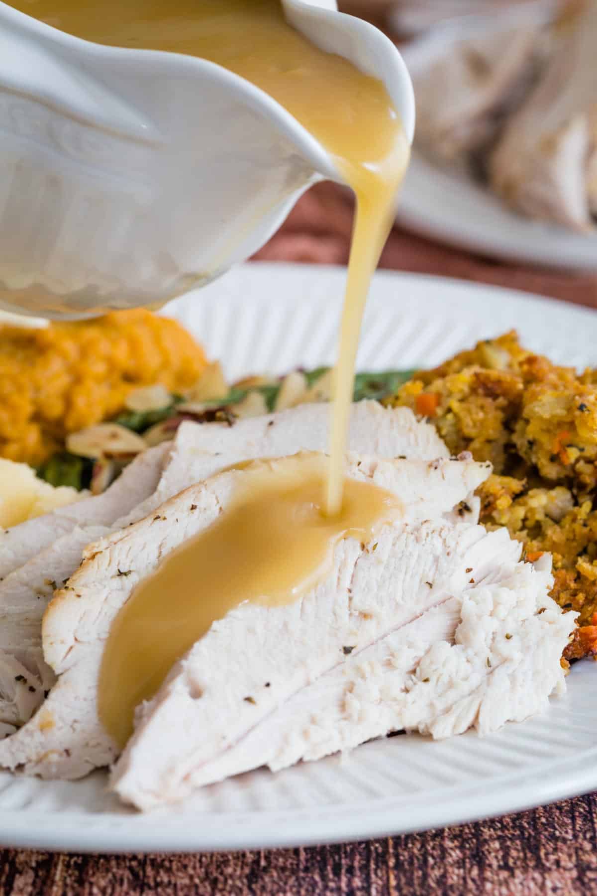 Gravy being poured out of a gravy boat over slices of turkey on a plate.