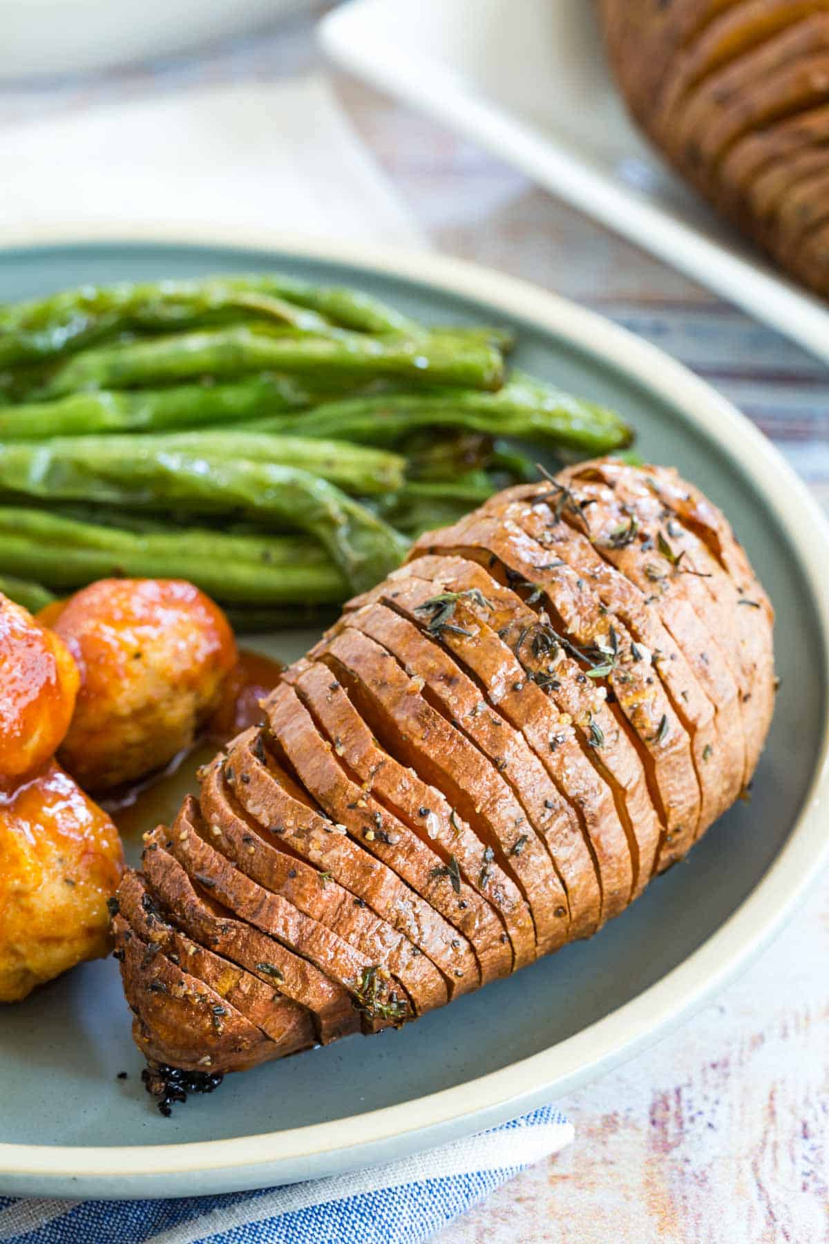 hasselback sweet potatoe on a plate with green beans