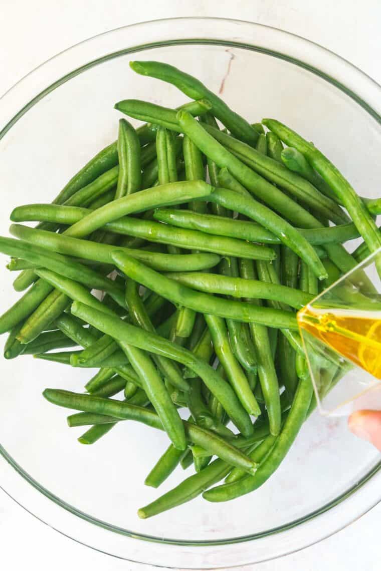 greeen beans in a bowl with olive oil pouring in