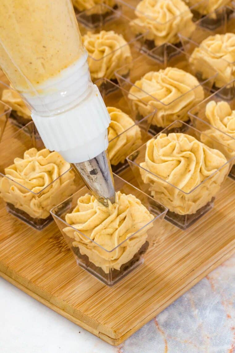 piping pumpkin mousse from a piping bag into the mini dessert cups