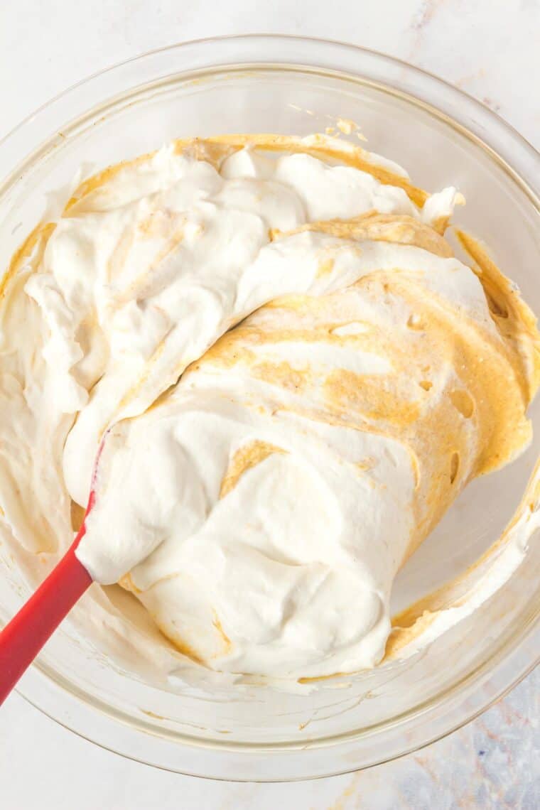 spatula folding whipped cream into the pumpkin cheesecake mousse base in a glass mixing bowl