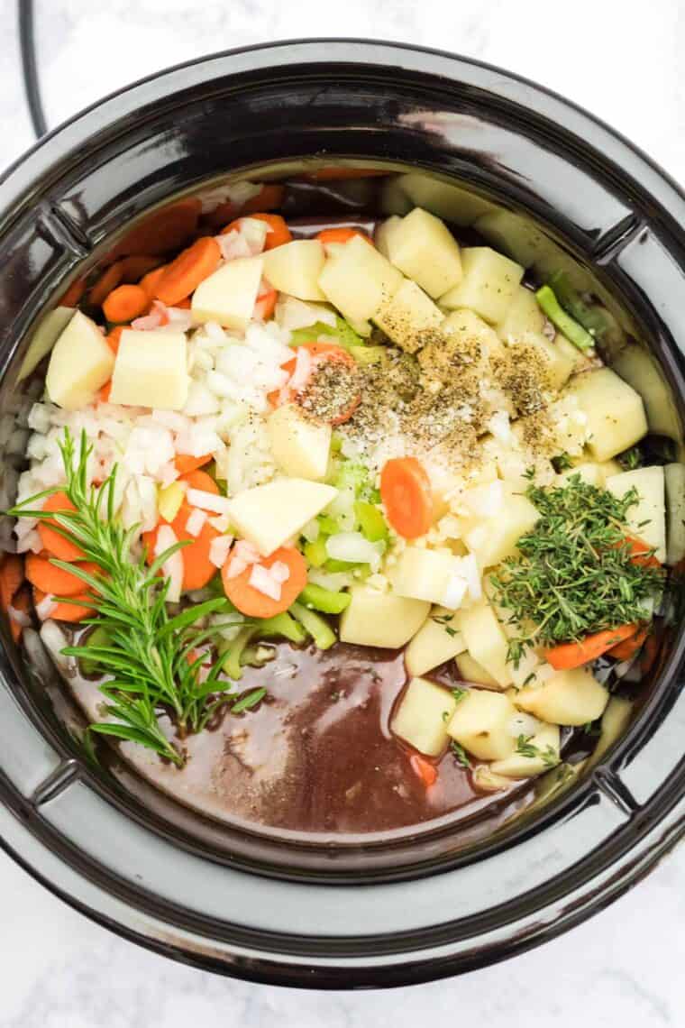 crockpot with carrots, onions, tomatoes, herbs and broth
