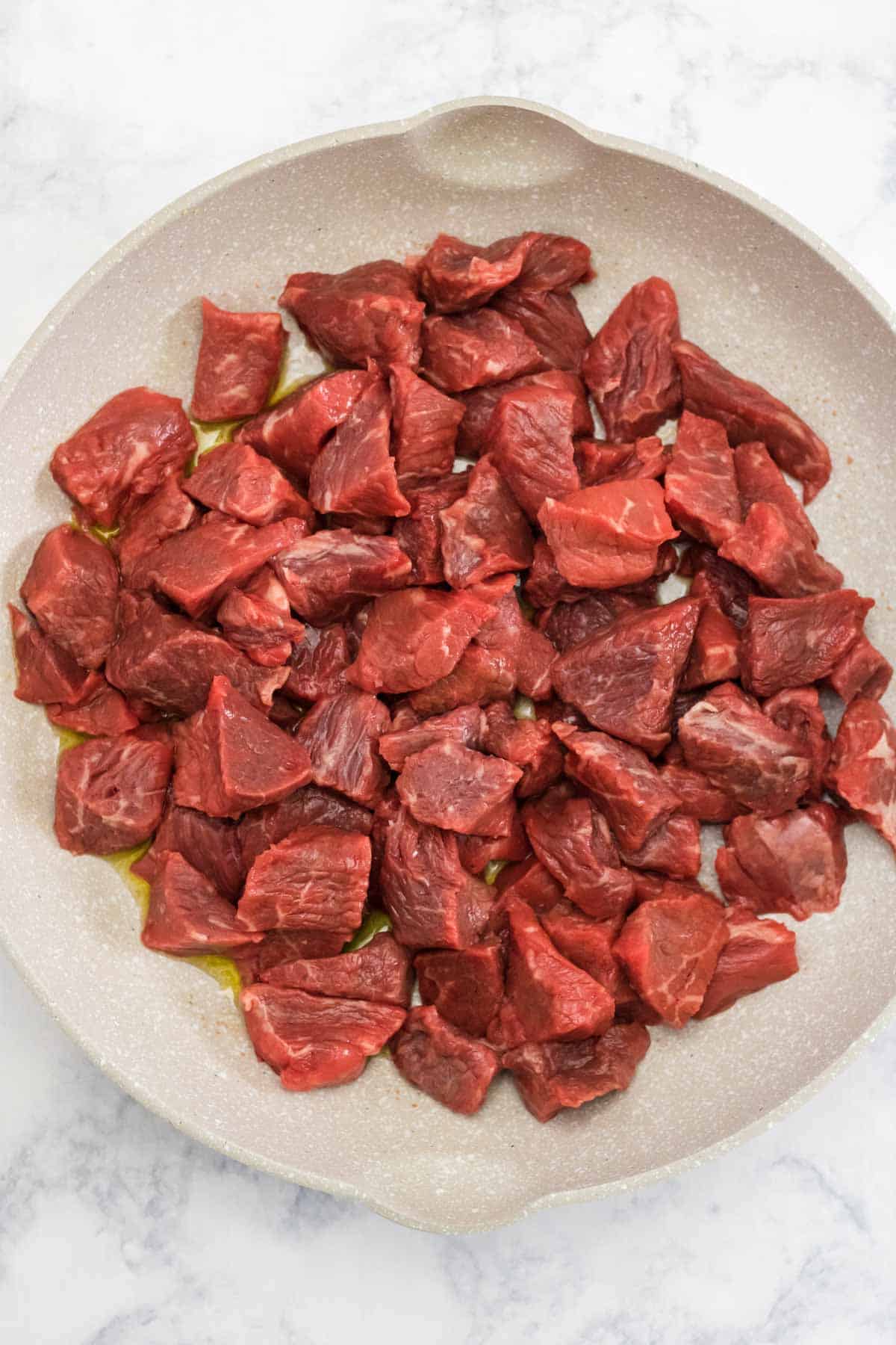 raw stew meat in a skillet