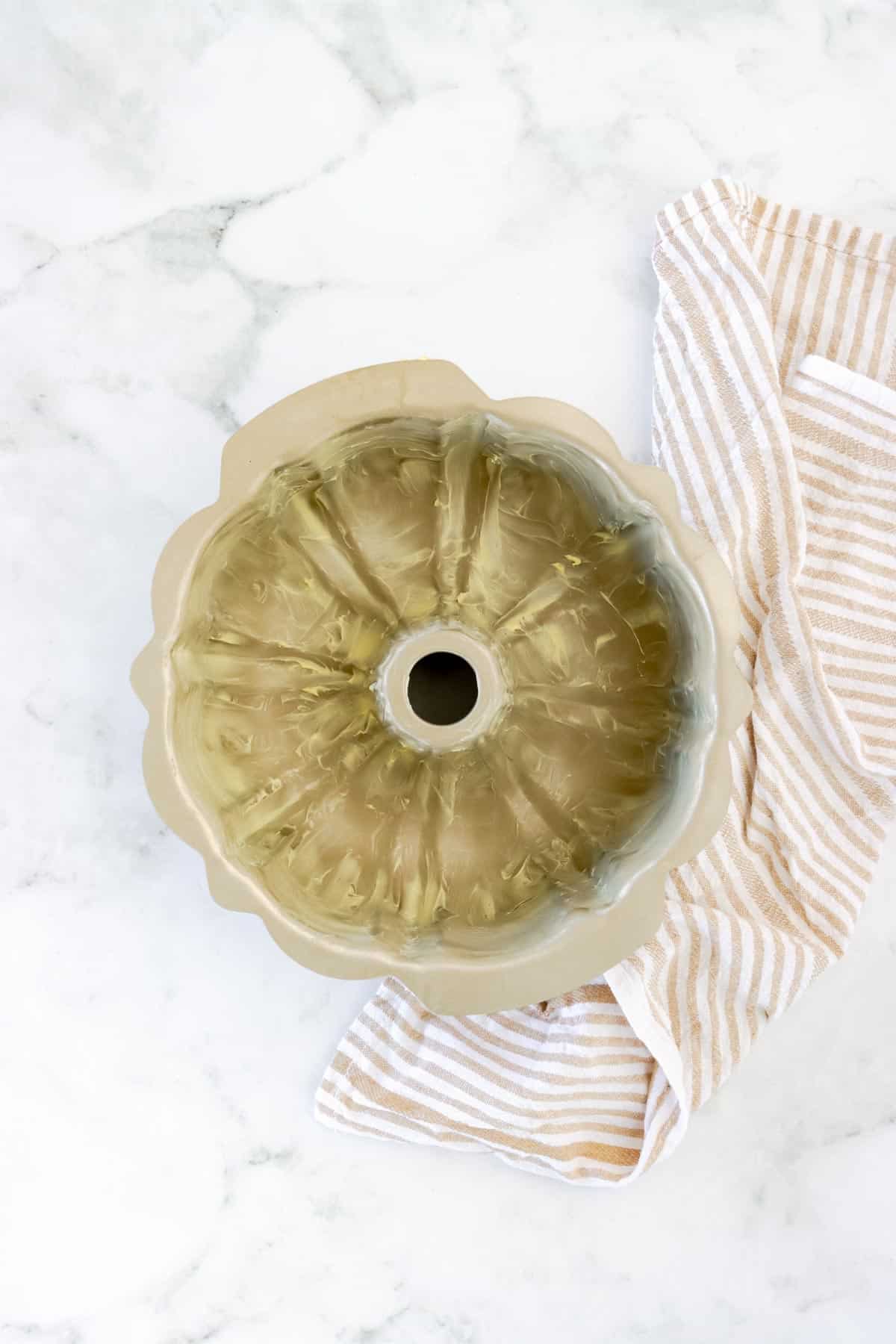 a greased bundt cake pan on top of a striped cloth napkin