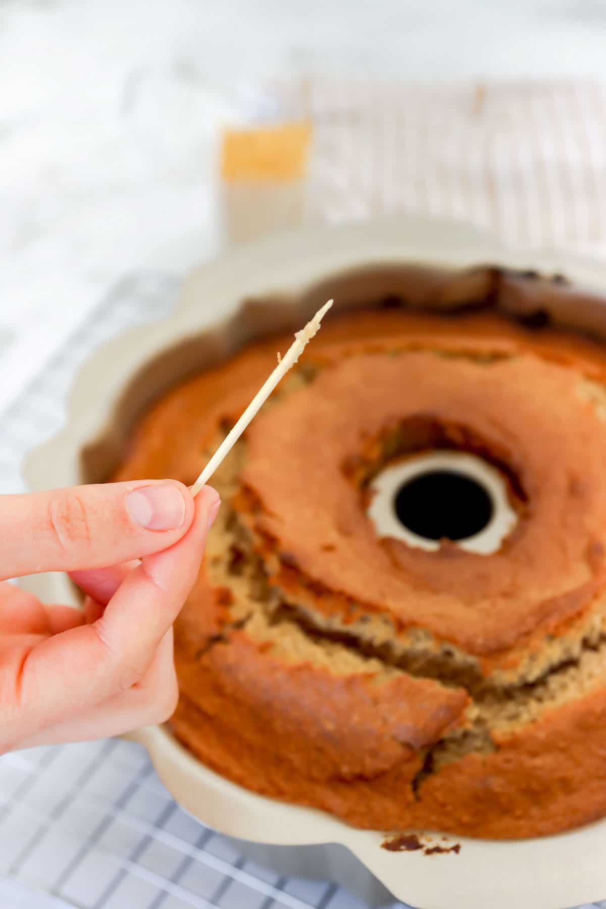 toothpick with just a few moist crumbs being held above a baked bundt cake