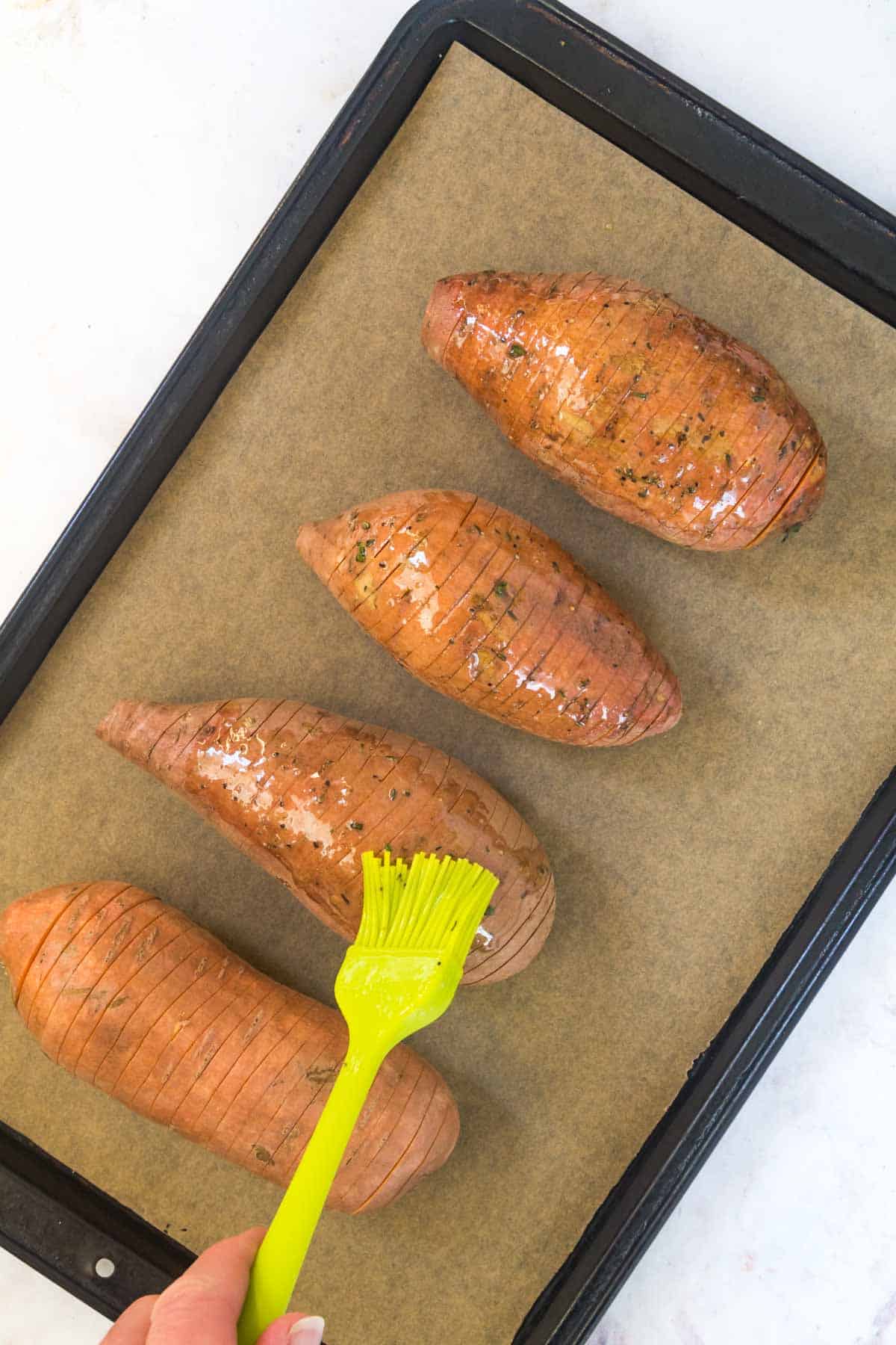 brushing sweet potatoes with honey butter on a baking sheet