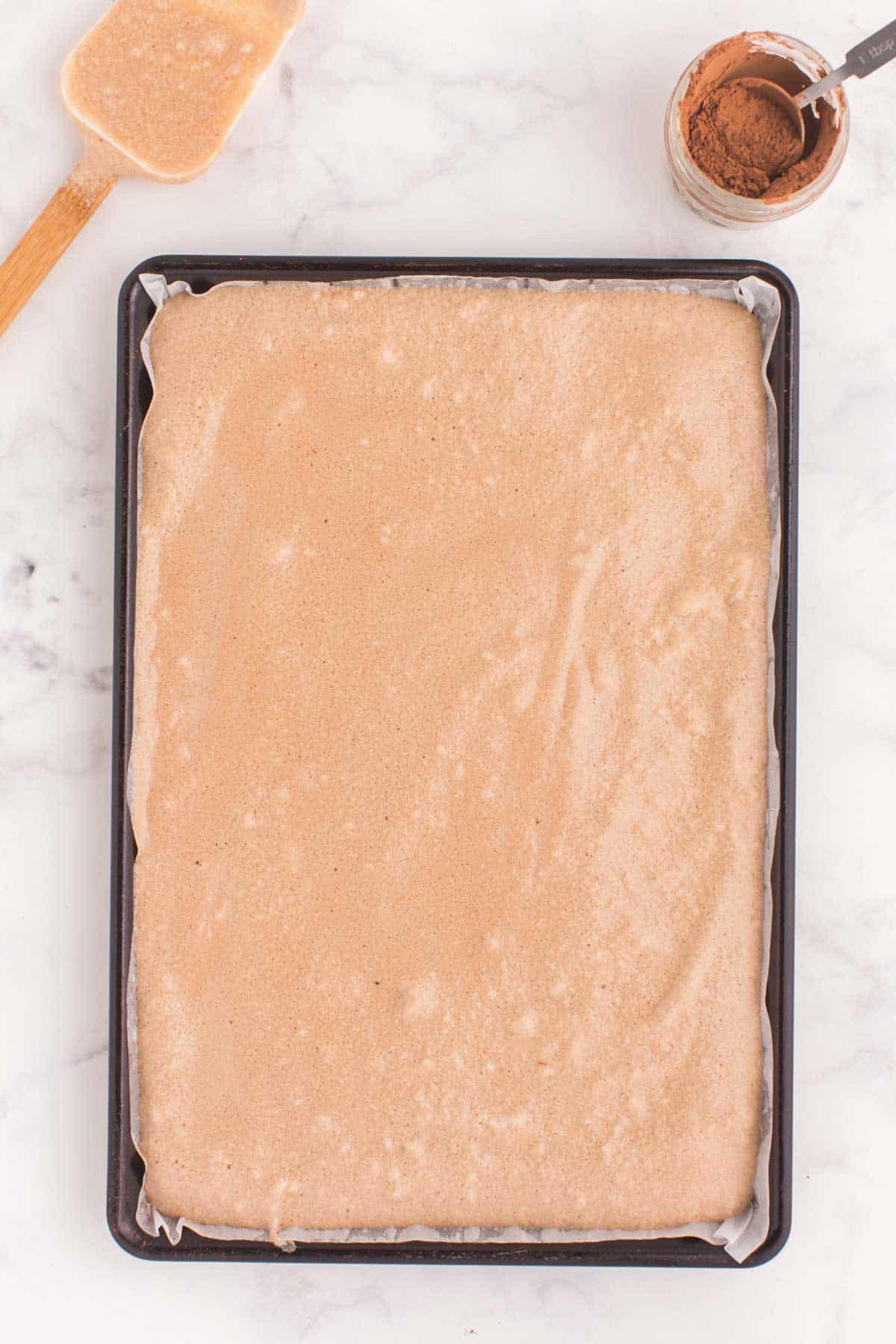 chocolate cake roll batter poured evenly into a parchment-lined baking sheet