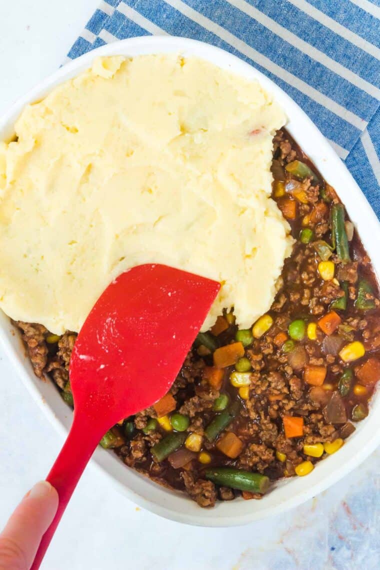spreading mashed potatoes on top of the shepherd's pie mixture