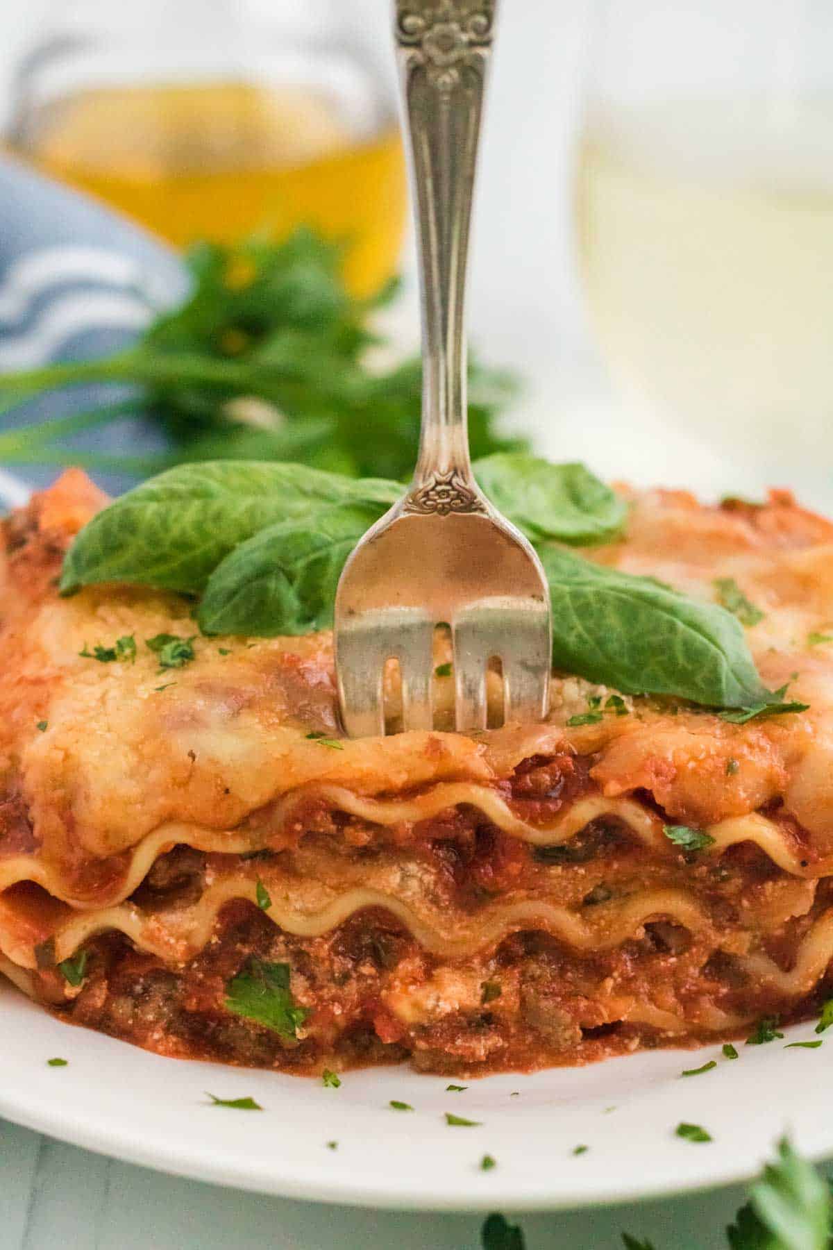 A fork standing up in a piece of lasagna on a plate.