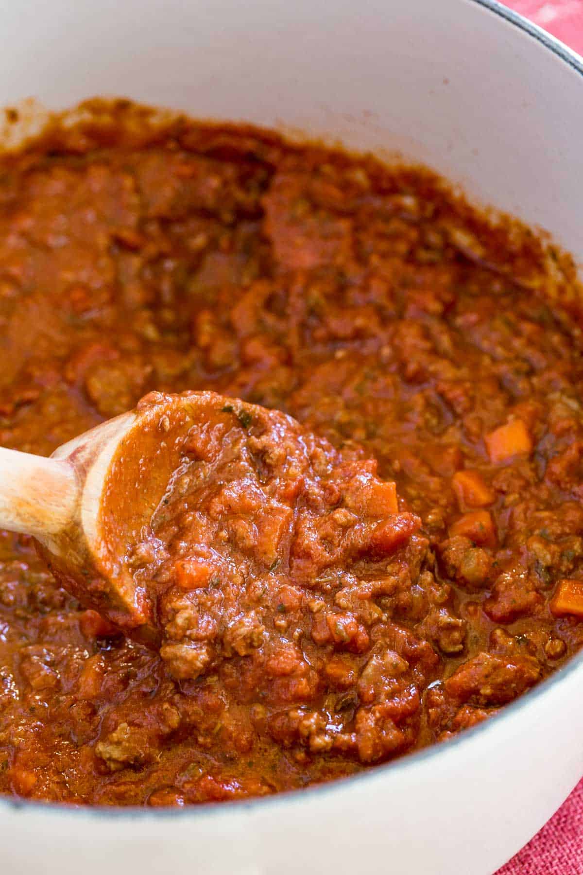 A wooden spoon in a pot of bolognese sauce.